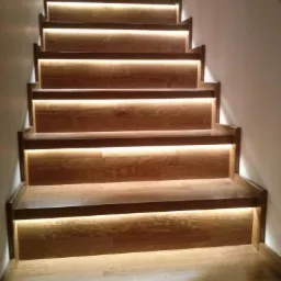 Drewniane schody z subtelnym podświetleniem LED pod każdym stopniem, ciepłe światło tworzy przytulną atmosferę.