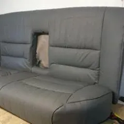 Szara, odnowiona tylna kanapa samochodowa z widocznym fragmentem starej tapicerki w miejscu otworu na podłokietnik.