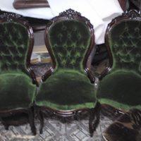 Trzy antyczne krzesła z ciemnozieloną, pikowaną tapicerką i rzeźbionymi, ciemnymi drewnianymi ramami, stojące obok siebie na podłodze wyłożonej jasnymi płytkami.