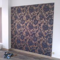 Ściana pokryta tapetą z motywem kwiatowym w odcieniach granatu i beżu. Widoczne narzędzia tapicerskie na podłodze.