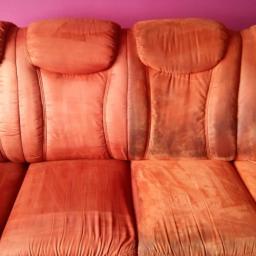 Pranie Tapicerek STG - Pomarańczowa kanapa z widoczną różnicą w czystości między wypraną częścią po lewej a brudną po prawej stronie na tle fioletowej ściany.