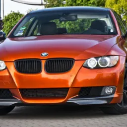 Pomarańczowe BMW serii 3 E92 z czarnymi felgami na tle zieleni, widok z przodu.