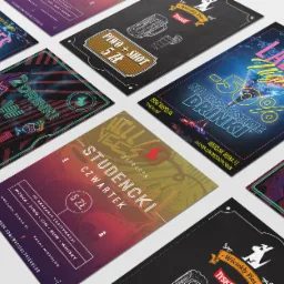 Różnorodne projekty graficzne, prawdopodobnie materiały promocyjne baru 'Wściekły Pies', przedstawiające oferty specjalne na drinki i piwo, ułożone pod kątem na jasnym tle.