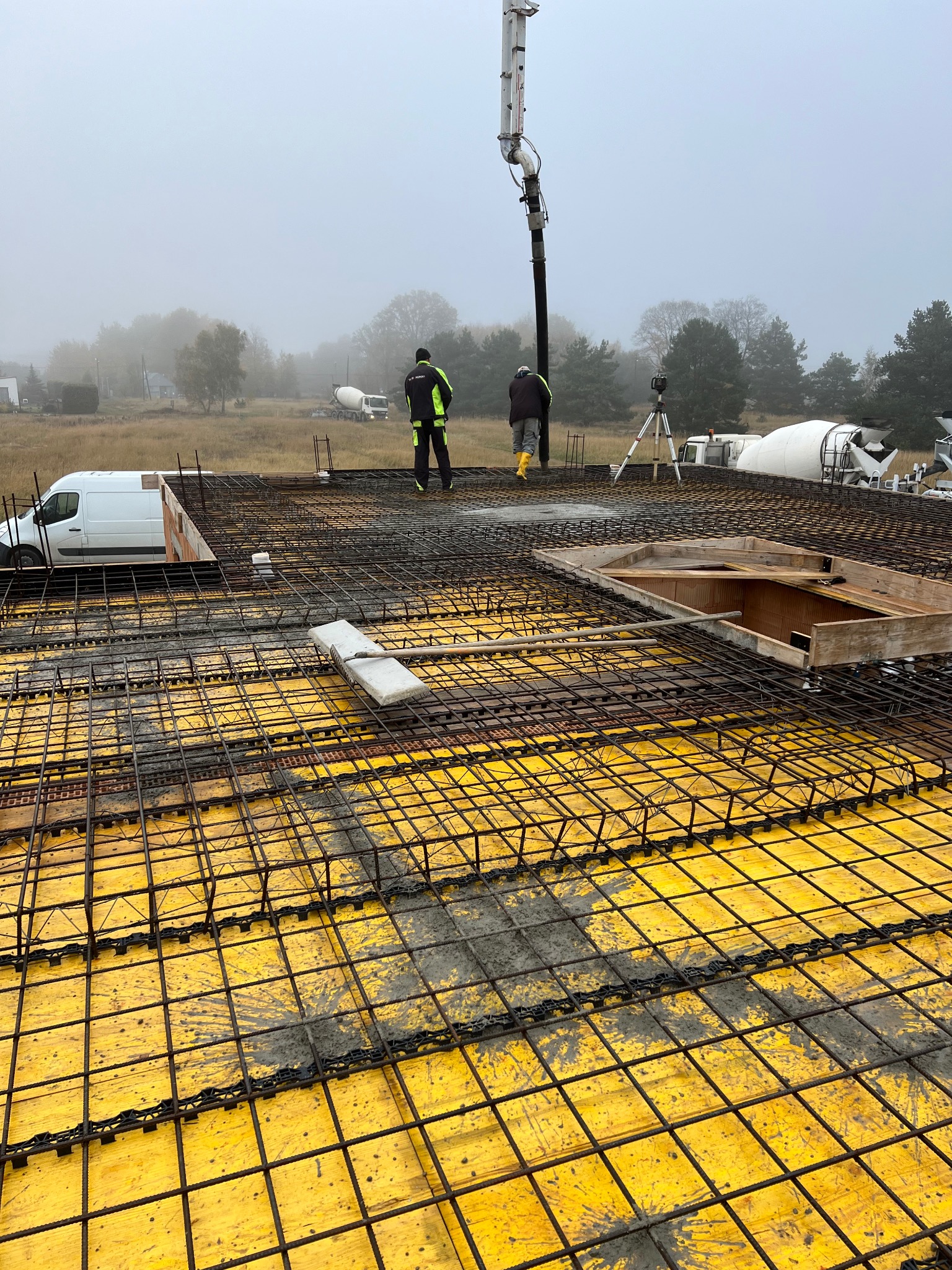 Zbrojenie stropu na żółtym szalunku, widoczni pracownicy i betonowóz w tle. Prace budowlane w Łęgach, 2024.
