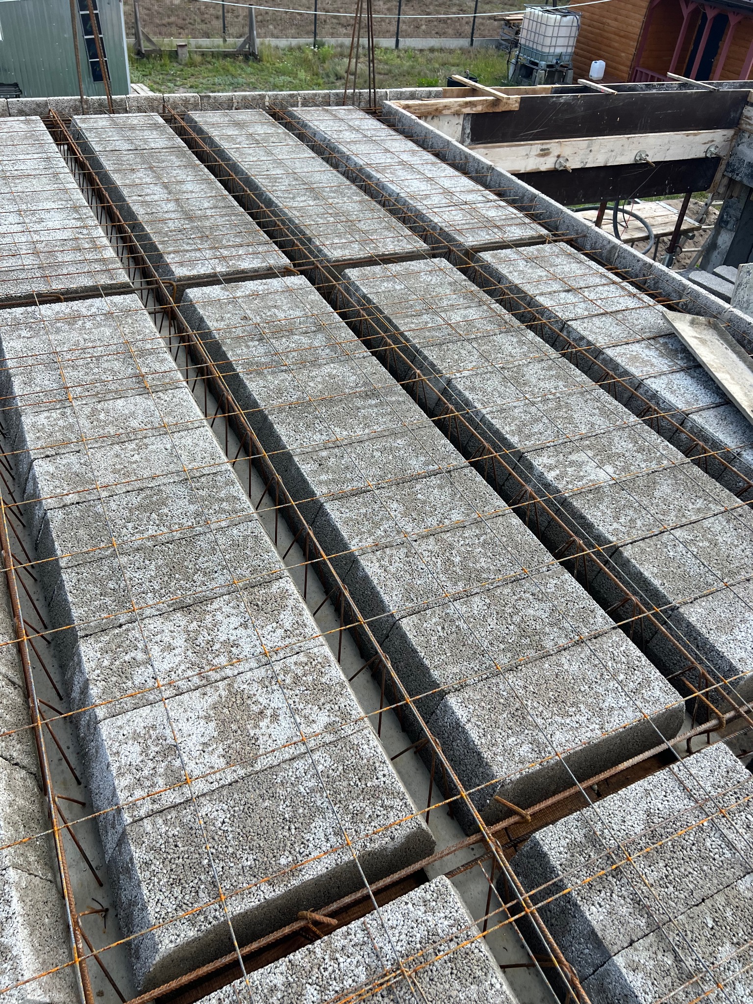 Wieniec stropowy z szalunkiem traconym i zbrojeniem, widok z góry. Element konstrukcyjny budynku w trakcie budowy, szare bloczki betonowe, stalowe pręty zbrojeniowe.