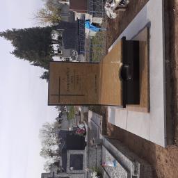 Kamieniarstwo Tomasz Wójcik - Nowoczesny nagrobek z jasnego kamienia z czarnymi elementami, umieszczony na cmentarzu, z widocznymi innymi nagrobkami w tle.