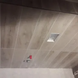 Płytki imitujące drewno ułożone na suficie, z widocznymi otworami na oświetlenie i elementami instalacji w trakcie montażu.