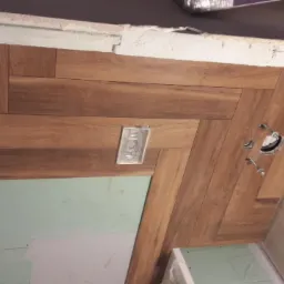 Układanie paneli podłogowych w jodełkę w łazience, widoczna instalacja elektryczna i fragment ściany z płyt gipsowo-kartonowych.