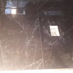 Błyszczące, czarne płytki imitujące marmur z białym żyłkowaniem, ułożone na podłodze w łazience w Komorowicach, z widocznym odpływem liniowym i elementami instalacji sanitarnej.