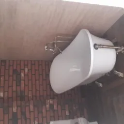 Biała wanna wolnostojąca na nóżkach w łazience z drewnianą podłogą ułożoną w jodełkę i ścianą wyłożoną cegłą.