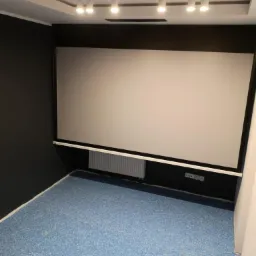 Pokój z zamontowanym ekranem projekcyjnym, oświetleniem punktowym i niebieską podłogą z tworzywa.