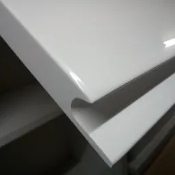 Detal uchwytu frezowanego w białym froncie szuflady z płyty MDF, widoczna krawędź blatu i wnętrze szafki.