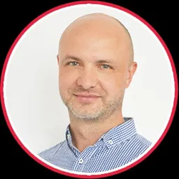 Portret mężczyzny z krótkimi włosami, w niebieskiej koszuli w kratę, uśmiechającego się do kamery, umieszczony w okręgu z czerwoną obwódką.