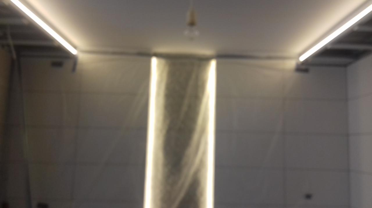 Świetlne akcenty w łazience: pionowy pas światła w ścianie i listwy LED pod sufitem, widoczna surowa żarówka na suficie.