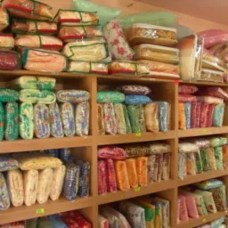 Półki wypełnione po brzegi zapakowanymi kompletami pościeli w różnych wzorach i kolorach, prawdopodobnie w hurtowni lub magazynie.