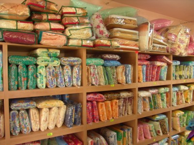 Półki wypełnione po brzegi zapakowanymi kompletami pościeli w różnych wzorach i kolorach, prawdopodobnie w hurtowni lub magazynie.