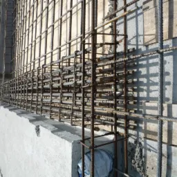 Zbrojenie fundamentu z betonu, widoczne stalowe pręty tworzące siatkę, szalunek z desek w tle, przygotowanie do wylania betonu.