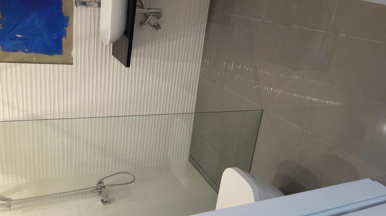 Nowoczesna łazienka z białą, falowaną płytką ścienną, szklaną kabiną prysznicową typu walk-in, wiszącą umywalką z czarną szafką i beżowymi płytkami podłogowymi.