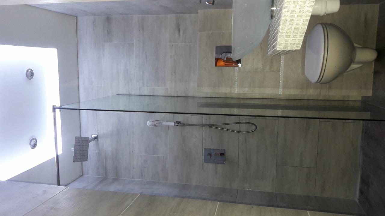 Nowoczesna łazienka z kabiną prysznicową typu walk-in, wykończona płytkami imitującymi drewno, z widoczną deszczownicą i panelem sterowania natryskiem.