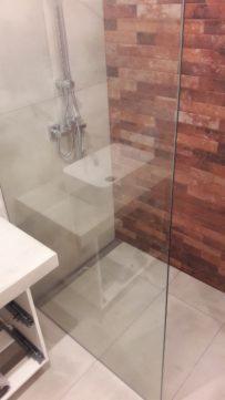 Nowoczesna kabina prysznicowa walk-in z chromowaną armaturą i białą umywalką na betonowym blacie, na tle ściany wyłożonej ceglastymi płytkami imitującymi cegłę.