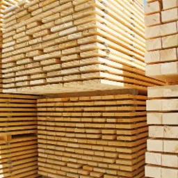 Stosy świeżo przetartej tarcicy budowlanej ułożone w równe warstwy, widoczne jasne drewno i regularny układ desek.