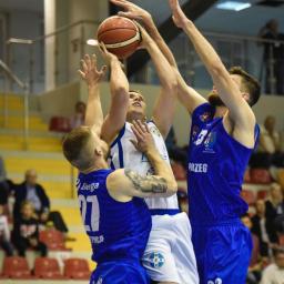 JMI Fotografia - Zawodnicy koszykówki w akcji podczas meczu, skok do kosza, piłka w powietrzu, dynamiczne ujęcie z hali sportowej.