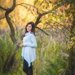 JMI Fotografia - Portret uśmiechniętej młodej kobiety w jesiennej scenerii, ubrana w jasnoniebieski sweter i czarne kozaki za kolano.