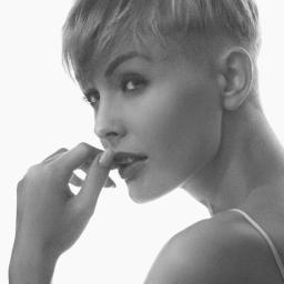 JMI Fotografia - Portret kobiety z krótkimi włosami, profil twarzy, czarno-białe zdjęcie z delikatnym oświetleniem, dłoń przy ustach, tatuaż na ramieniu.