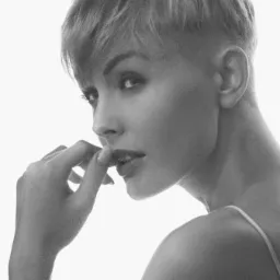 Portret kobiety z krótkimi włosami, profil twarzy, czarno-białe zdjęcie z delikatnym oświetleniem, dłoń przy ustach, tatuaż na ramieniu.