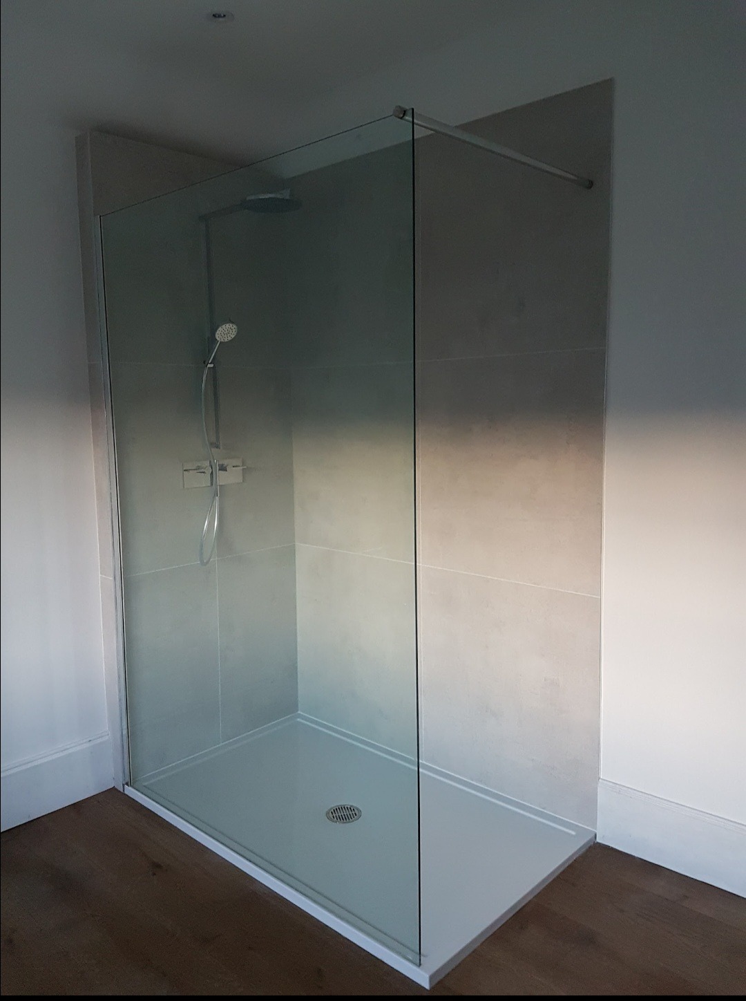 Nowoczesna kabina prysznicowa walk-in z szarymi płytkami, minimalistyczną armaturą i odpływem liniowym, osadzona na drewnopodobnej podłodze.