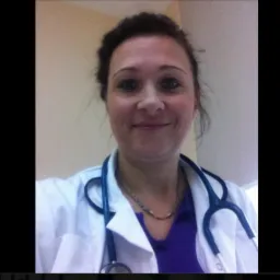 Portret uśmiechniętej kobiety w białym fartuchu medycznym i stetoskopie na szyi, w jasnym wnętrzu.