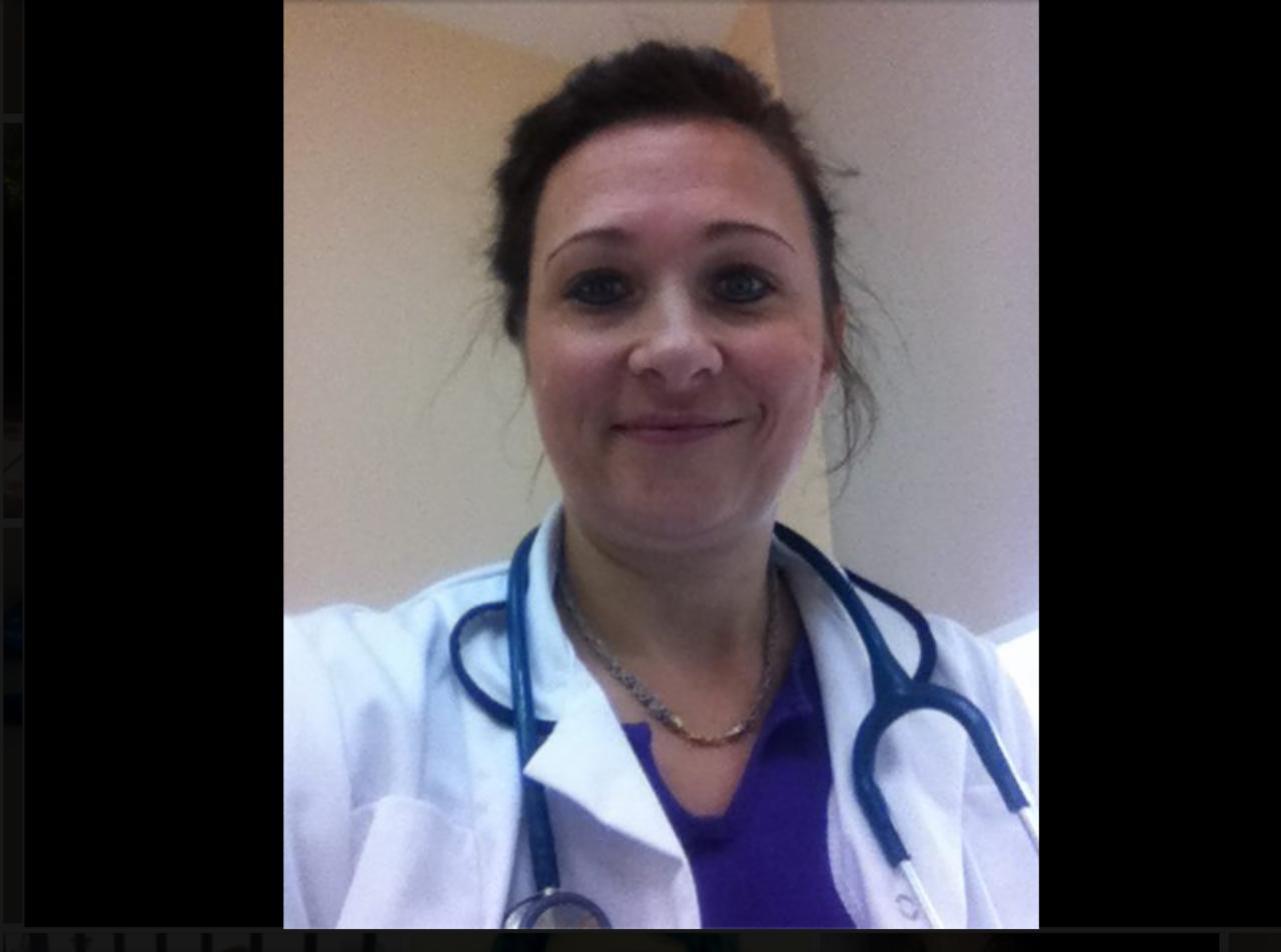 Portret uśmiechniętej kobiety w białym fartuchu medycznym i stetoskopie na szyi, w jasnym wnętrzu.