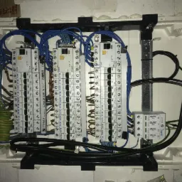 Otwarta skrzynka rozdzielcza z bezpiecznikami i okablowaniem, widoczne elementy marki Eaton i Simtec, montaż w surowym stanie.
