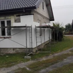 Dom w Hruszowie w trakcie ocieplania elewacji styropianem, widoczne rusztowania i niezabezpieczone okna.