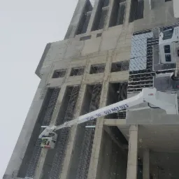 Montaż zbrojenia na wysokości w surowym budynku z użyciem podnośnika koszowego w zimowy dzień.