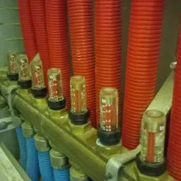 Rozdzielacz instalacji grzewczej podłogowej z rzędami czerwonych i niebieskich rur karbowanych, z zamontowanymi przepływomierzami, widok z bliska.