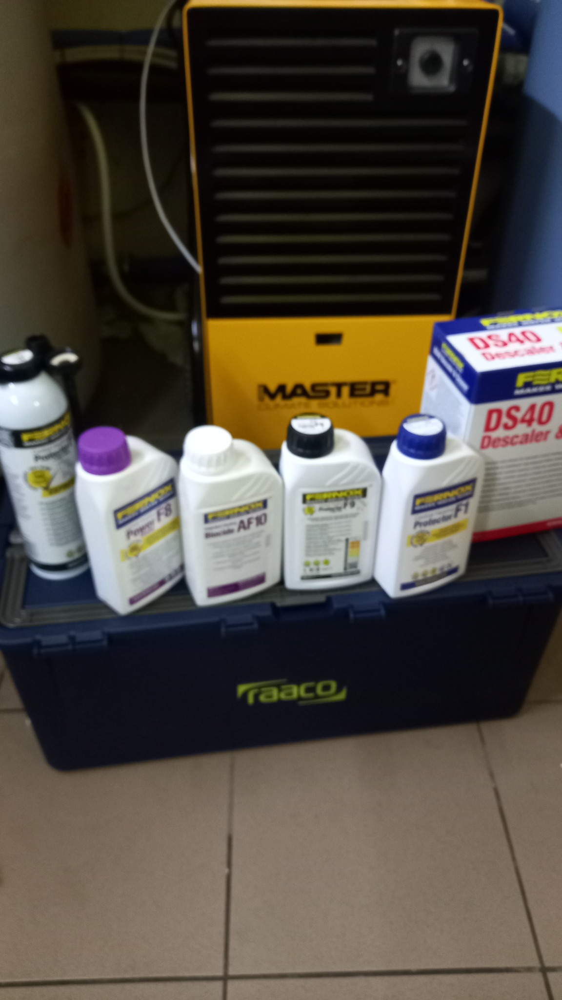 Preparaty chemiczne do czyszczenia i konserwacji systemów klimatyzacji i wentylacji, ustawione na niebieskiej skrzynce narzędziowej marki Raaco, z żółtym osuszaczem powietrza Master w tle.