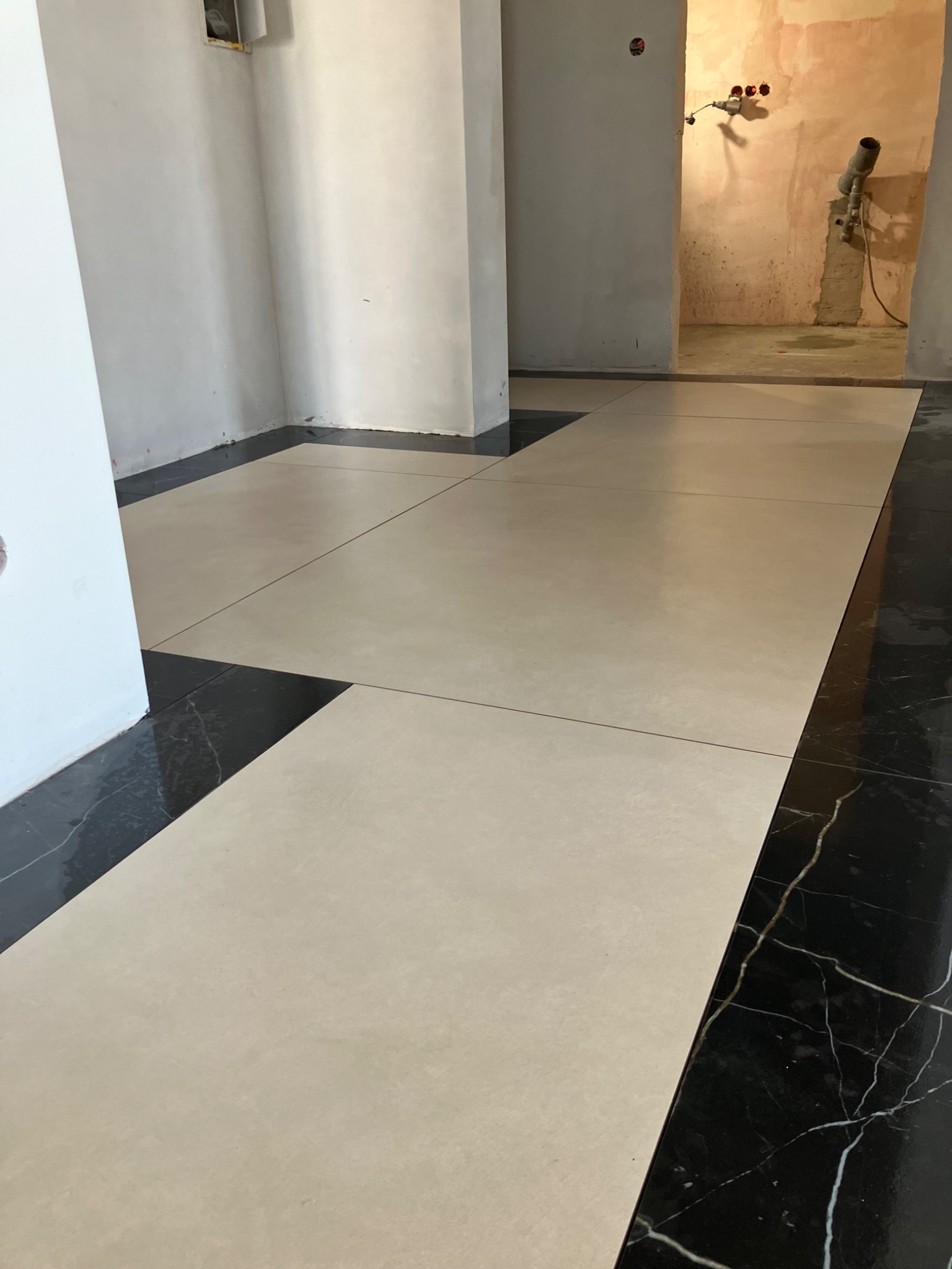 Ułożona podłoga z jasnych, kwadratowych płytek z czarnym marmurowym obramowaniem w trakcie prac wykończeniowych w lokalu w Zielonej Górze.