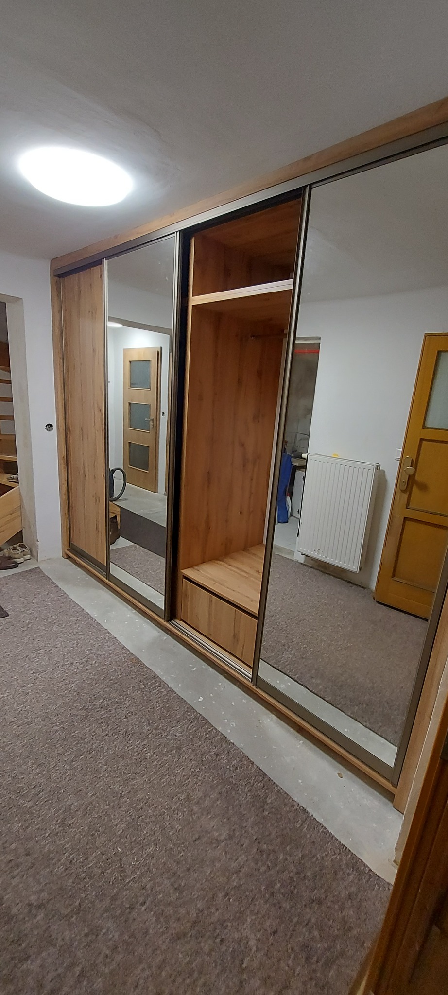 Duża szafa przesuwna z lustrzanymi drzwiami i drewnianym wykończeniem, widoczna w pokoju z brązowym dywanem i odblaskami wnętrza.