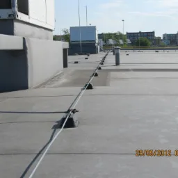 System odgromowy z przewodami na dachu budynku, widoczne elementy mocujące i przewody uziemiające, w tle zabudowa miejska.