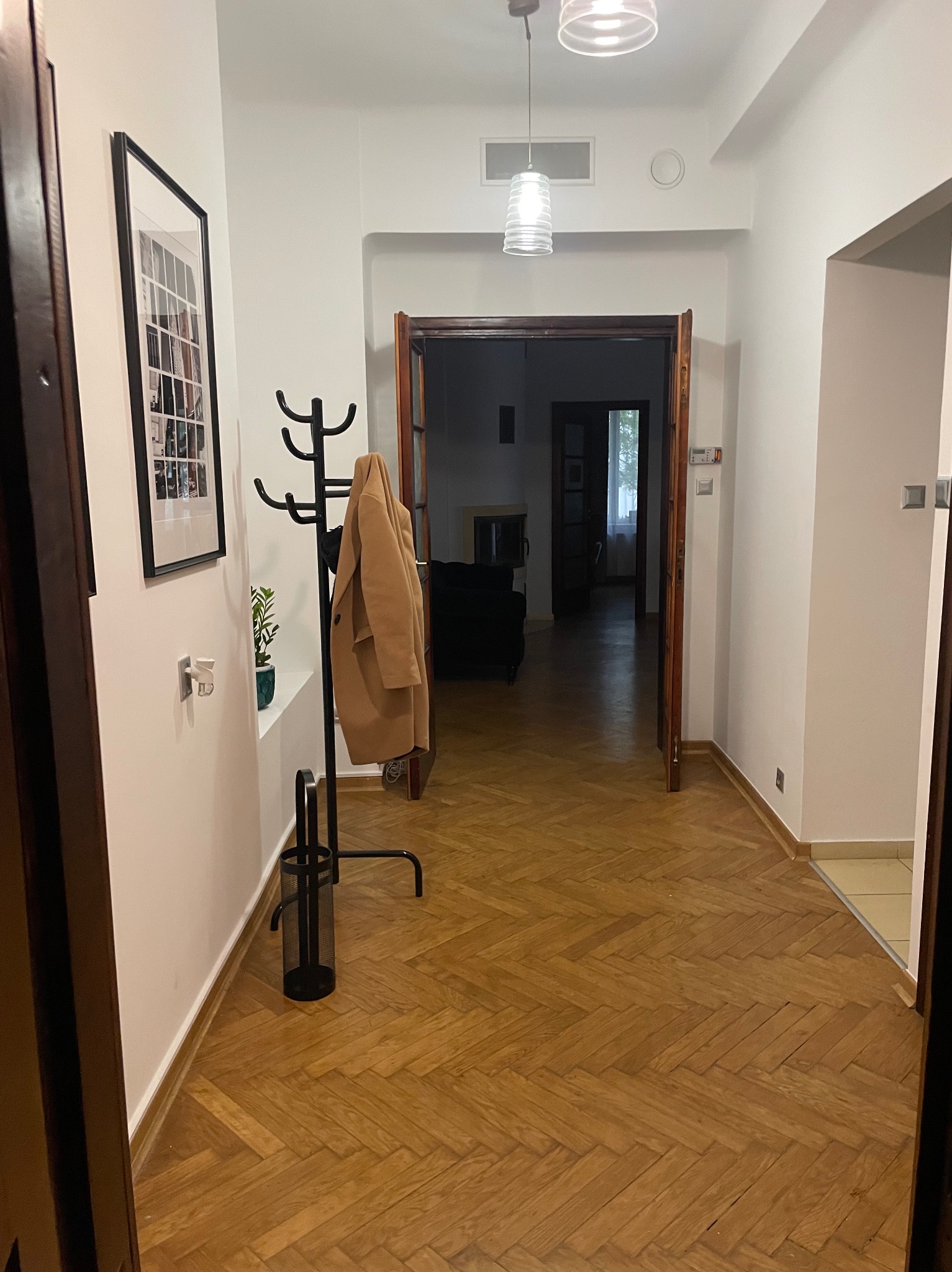 Wnętrze korytarza z parkietem w jodełkę, wieszakiem na ubrania z płaszczem i obrazem na ścianie.