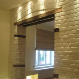 Wykończone przejście w ścianie z dekoracyjną cegłą w odcieniach beżu, z drewnianymi elementami nadproża i kolumny, widok na okno z roletą rzymską.