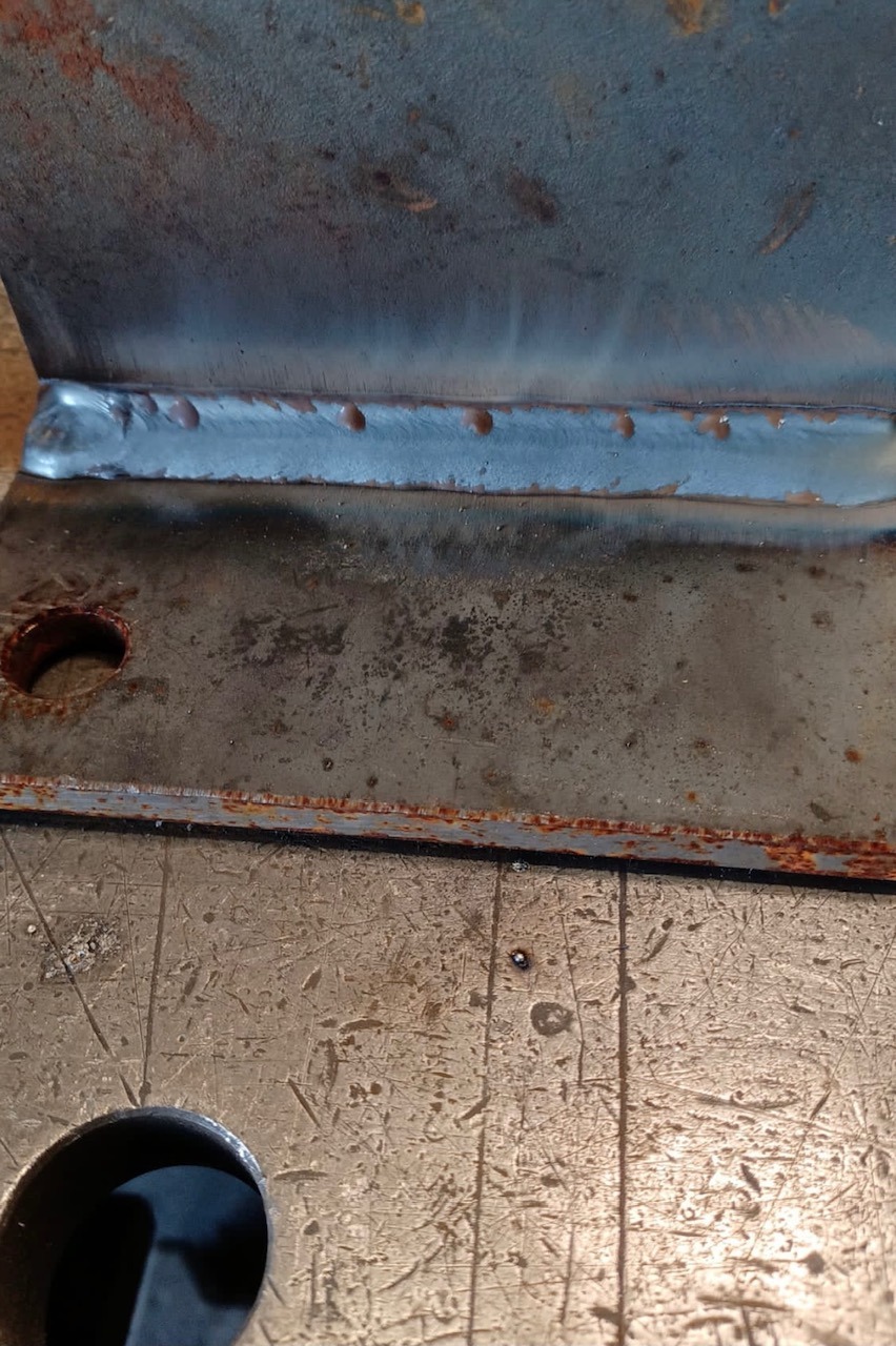Spoina na zardzewiałych elementach metalowych, widoczne ślady obróbki i otwór montażowy.