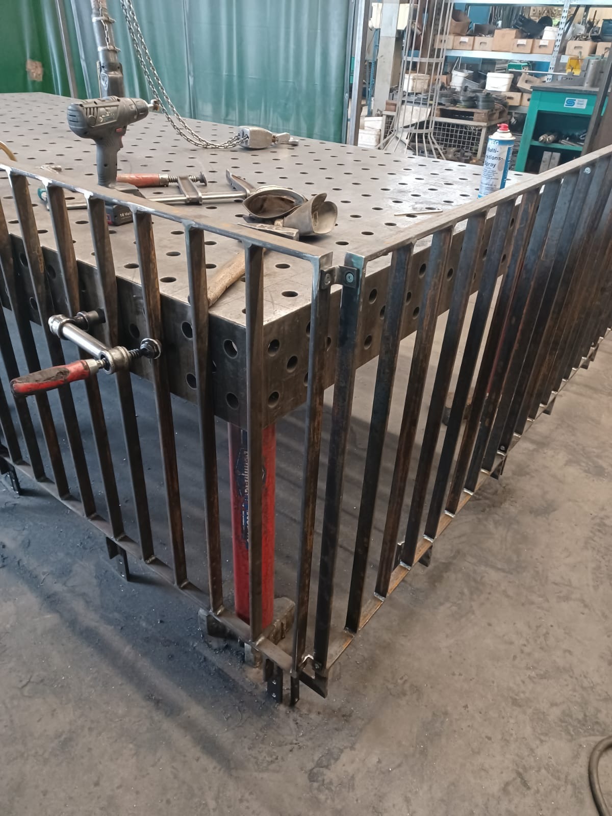 Spawana metalowa konstrukcja balustrady na perforowanym stole spawalniczym z narzędziami, widoczne ślady spawania, w tle warsztat.