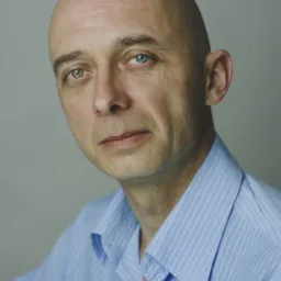 Portret mężczyzny z heterochromią, w błękitnej koszuli, na szarym tle. Ujęcie od przodu, skupione na twarzy i różnobarwnych oczach.