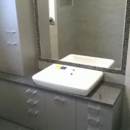 Szara zabudowa łazienkowa z szafkami i umywalką nablatową w Serokomli, z lustrem w ramie z mozaiki i toaletą.