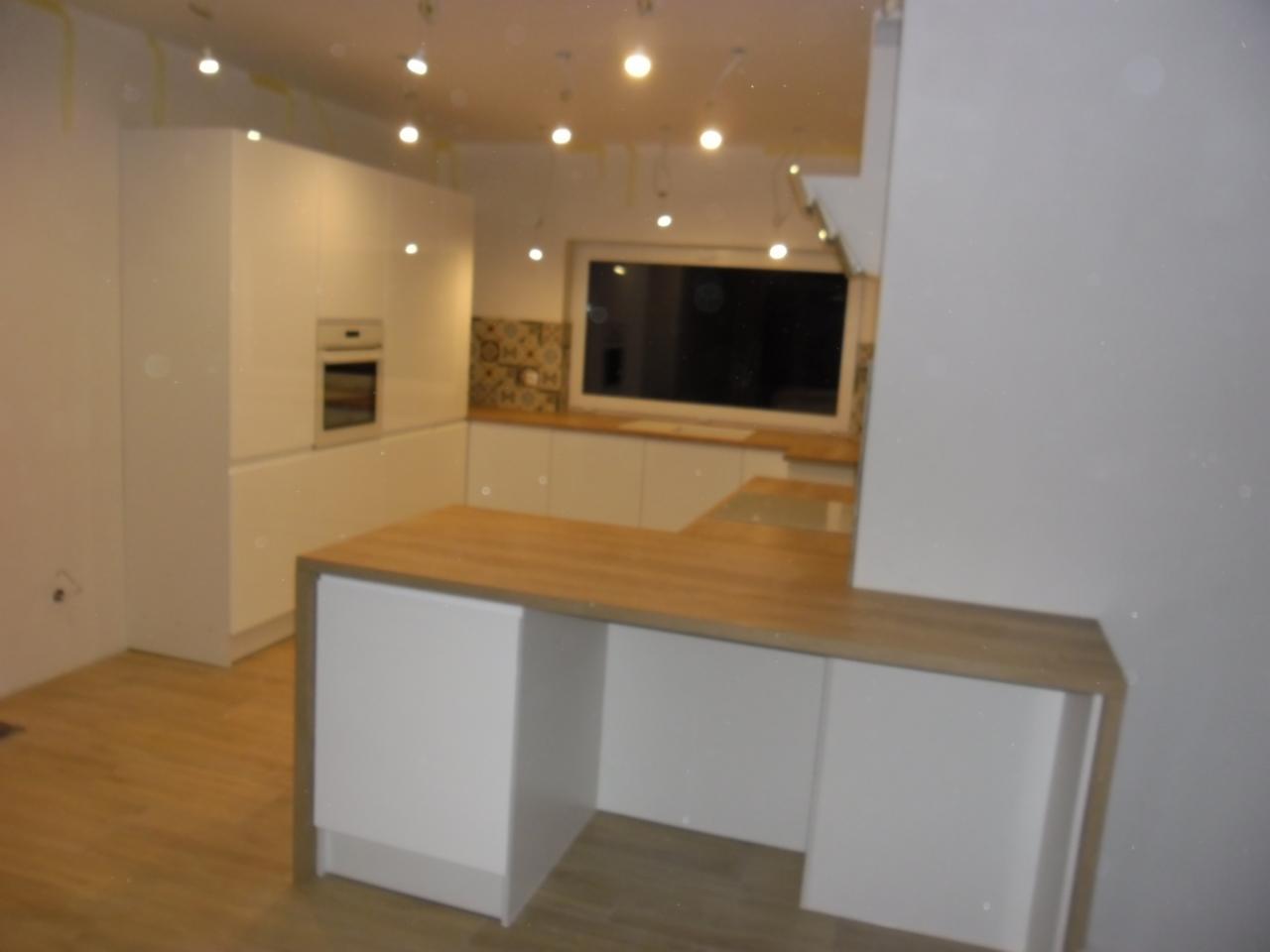 Nowoczesna, biała kuchnia z drewnianym blatem, oświetleniem punktowym i oknem z widokiem na zewnątrz, w trakcie wykańczania, widoczne ślady po pracach remontowych.