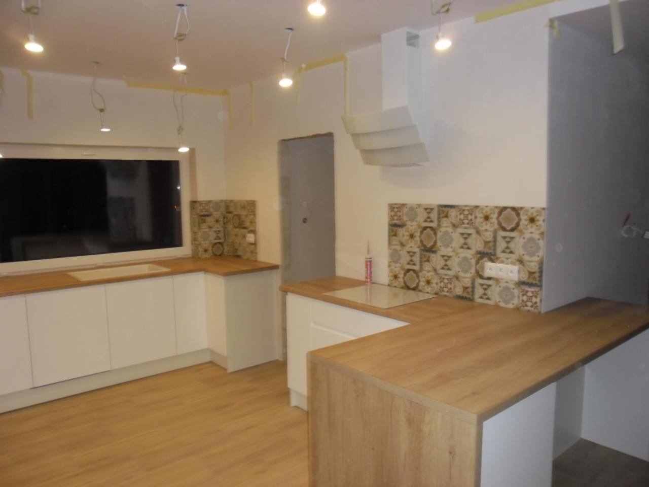 Wnętrze kuchni w trakcie montażu w Serokomli, widoczne białe szafki z drewnianym blatem i fragmentem okładziny ściennej z wzorzystych płytek.