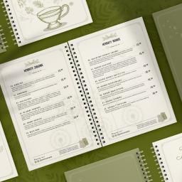 Falcontent - Otwarty, spiralny, dwustronicowy jadłospis herbat w odcieniach zieleni, z ilustracjami ziół i dmuchawców, prezentujący ziołowe i rooibos kompozycje.