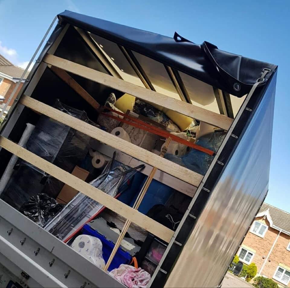 Wnętrze skrzyni ładunkowej samochodu transportowego, wypełnione różnorodnymi przedmiotami zabezpieczonymi pasami, widok z dołu pod kątem, jasne niebo w tle.